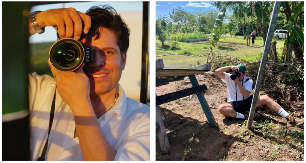 Un hombre sonriente sostiene una cámara Leica y mira a través de ella. Está vestido con una camisa blanca y se encuentra al aire libre.