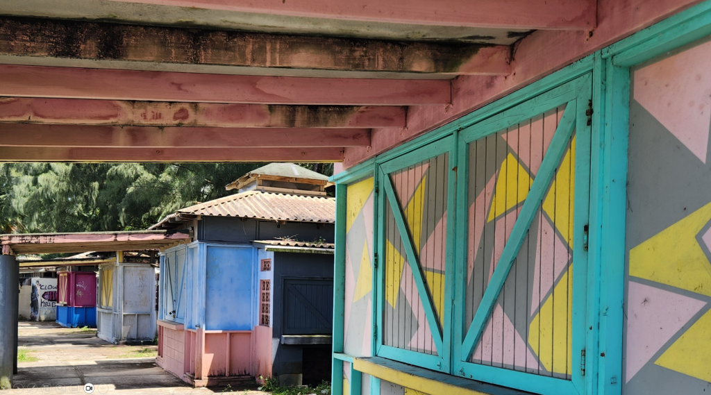 Vista de un pasillo con casas de colores brillantes y diseños geométricos en las puertas, rodeadas de naturaleza.